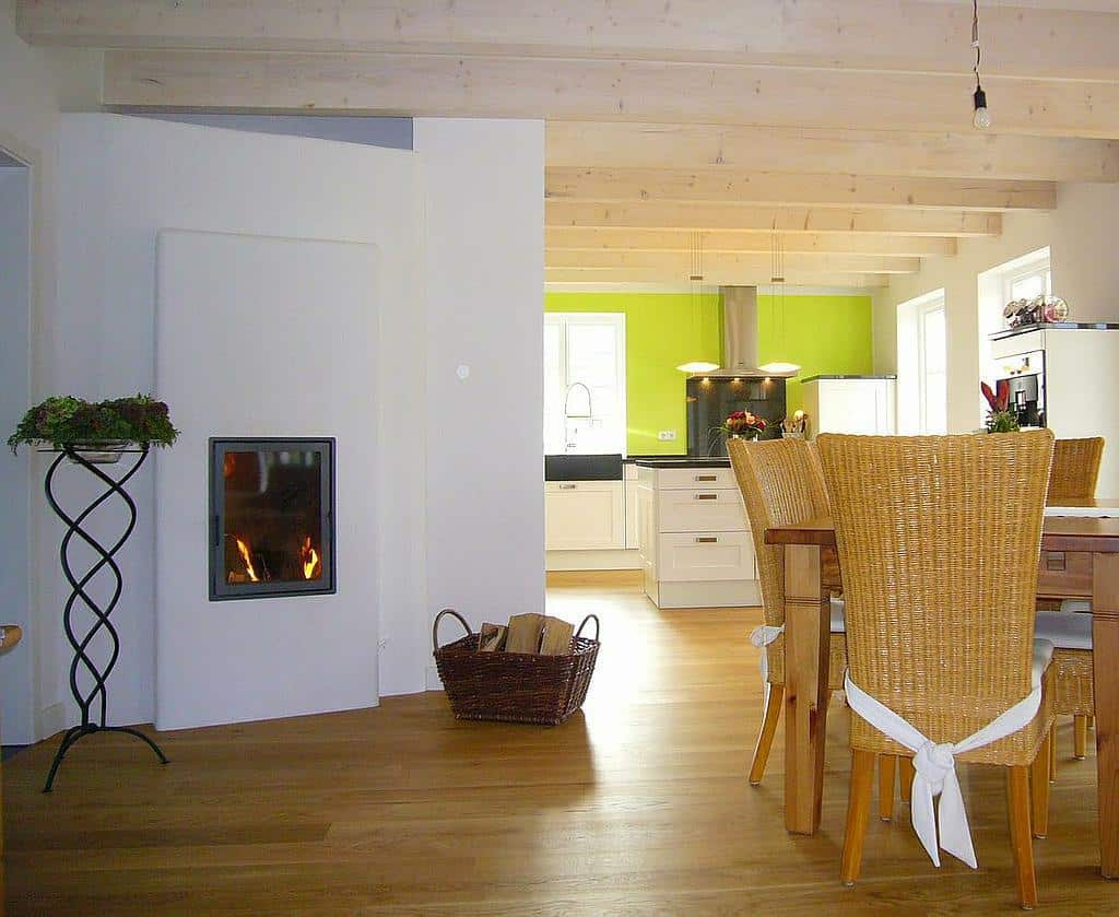 Schlichter Speicherofen in offenem Wohn-Essbereich mit Holzboden, Sichtbalkendecke und grüner Küchenwand
