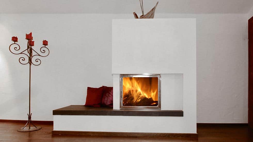Moderner Kaminofen mit integrierter Sitzbank in schlichtem Wohnraum mit Holzfußboden und Kerzenständer