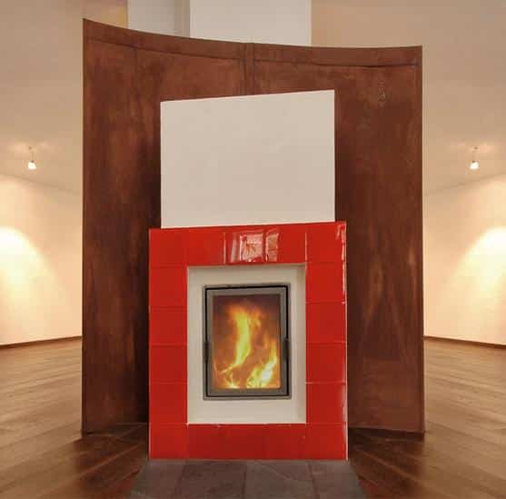 Moderner Kamin mit roter Kachelverkleidung vor geschwungener Roststahlwand in leerem Raum mit Holzfußboden