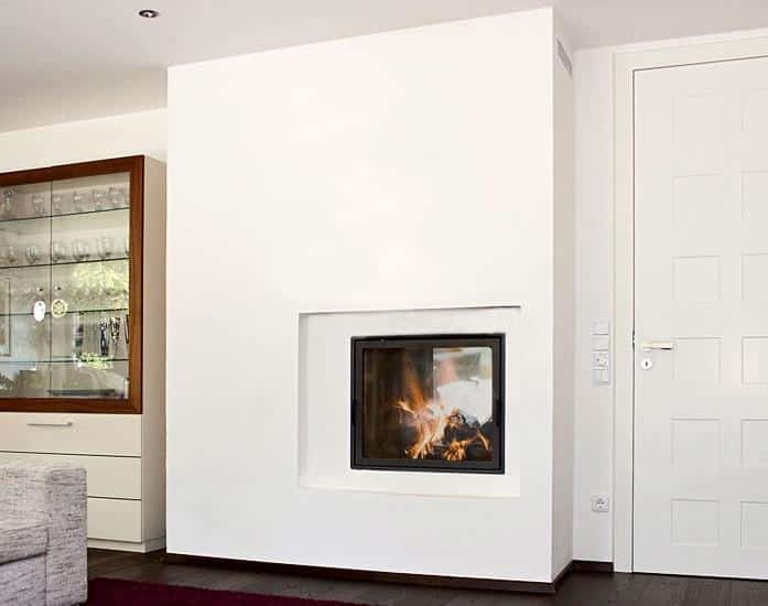 Schlichter Kaminofen mit verputzter Oberfläche in modernem Wohnraum mit Vitrine und dunklem Holzboden