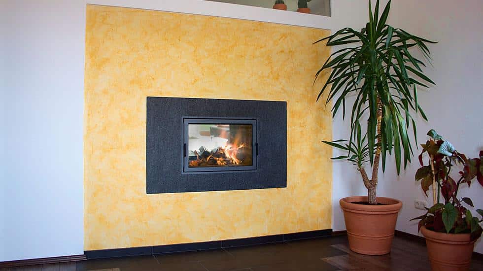 Kamin mit schwarzer Einfassung in sonnengelb gestalteter Wand und Zimmerpflanzen in modernem Wohnraum