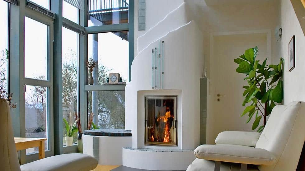 Kamin mit organischer Putzform in modernem Wintergarten mit großer Glasfront, Sitzbank und Zimmerpflanzen