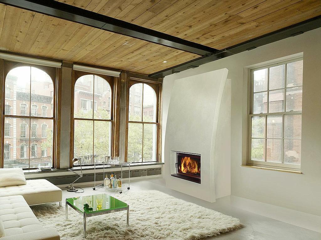 Moderner Designkamin mit geschwungener Verkleidung in hellem Loft mit großen Bogenfenstern und Holzdecke