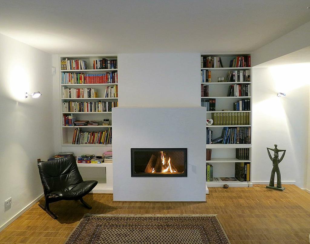 Moderner Kaminofen in Wohnzimmer mit Einbauregalen, Bücherwand und gemütlichem Lesesessel