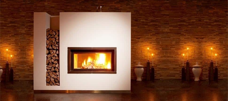 Moderner Kamin mit Holzlager vor rustikaler Steinwand und stimmungsvollem Kerzenlicht