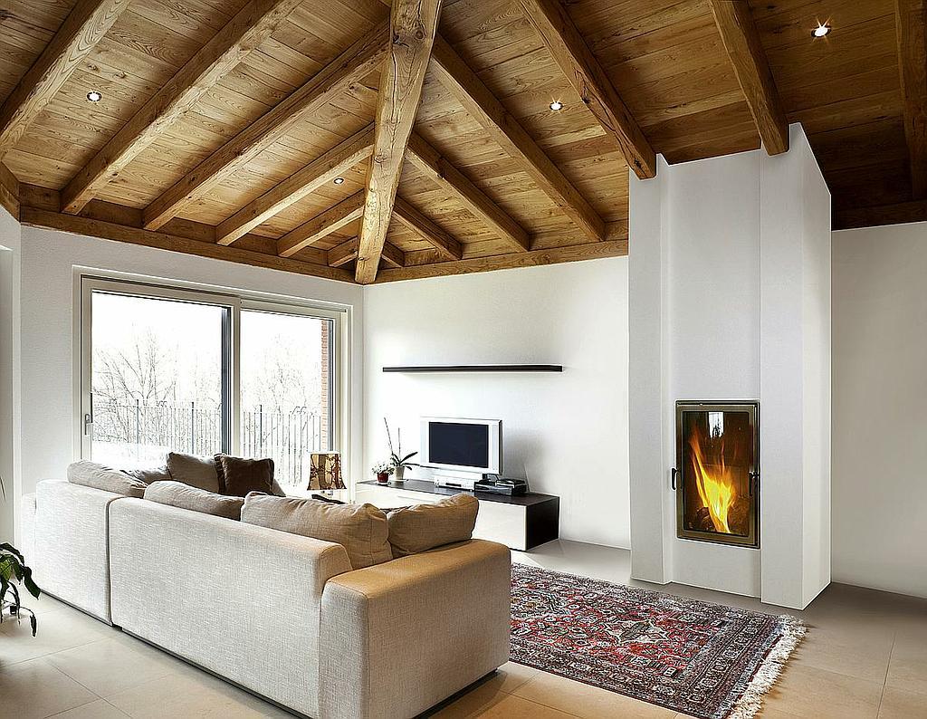 Moderner Kaminofen mit hoher Feuerraumtür in hellem Wohnraum mit Holzbalkendecke und großer Fensterfront