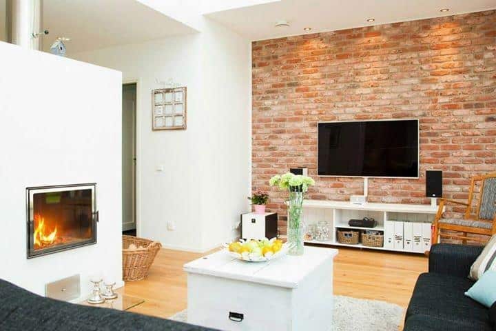 Moderner Kaminofen mit Edelstahlrahmen in hellem Wohnzimmer mit Backsteinwand und TV