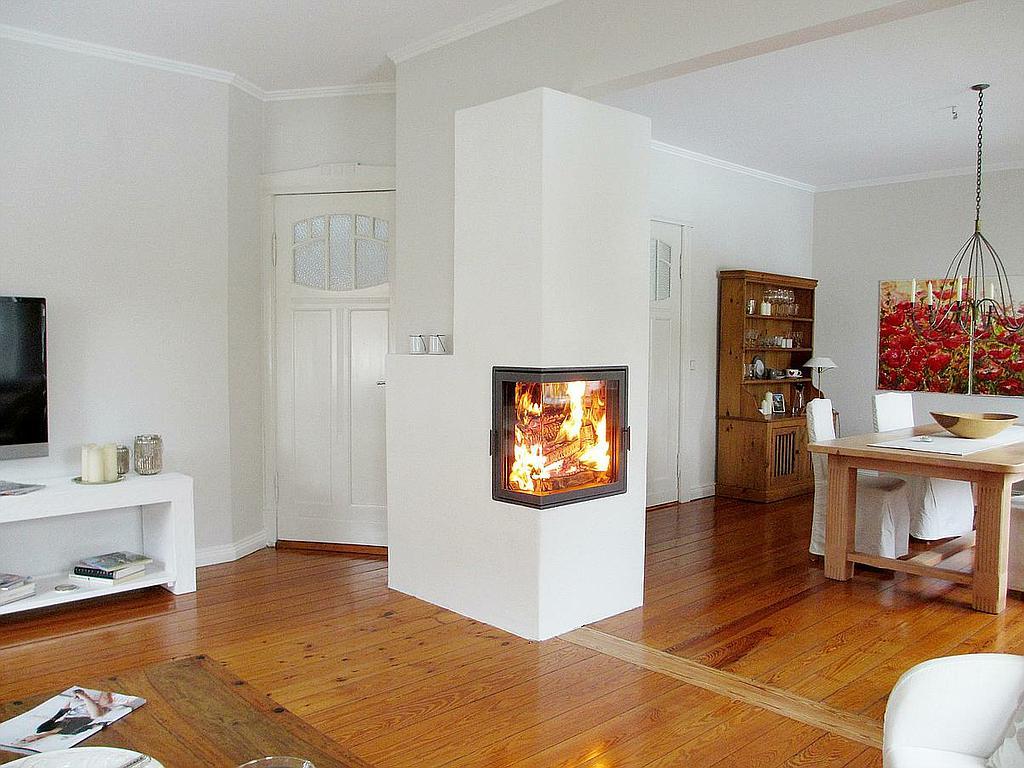 Raumteiler-Kamin mit Durchsicht in hellem Wohn-Essbereich mit Holzboden und weißen Wänden