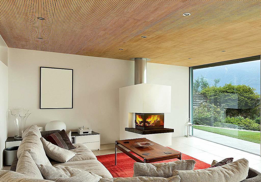 Moderner freistehender Kamin mit Glasfront in hellem Wohnzimmer mit Panorama-Fenster und Holzdecke