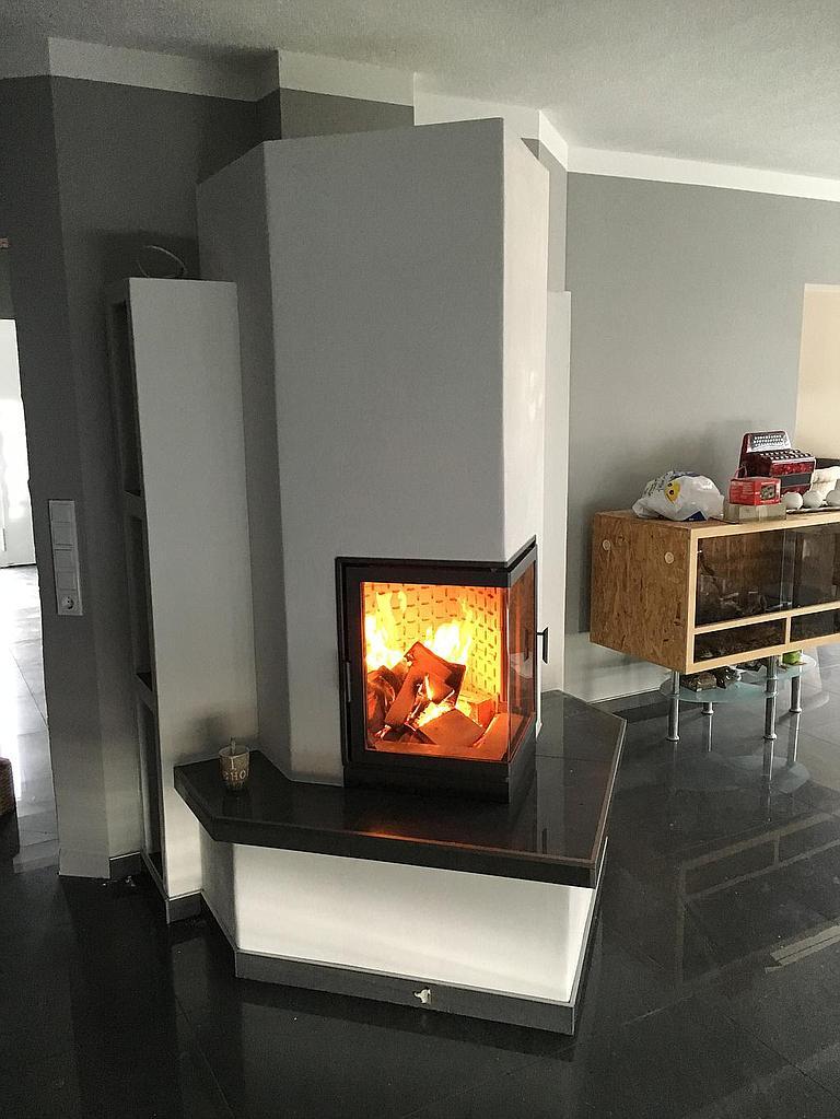 Moderner Speicherofen mit dunkler Abdeckplatte und prismatischer Form in grauem Wohnambiente