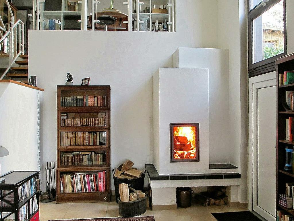 Moderner Speicherkamin in weißem Design neben einem Bücherregal, Flammen sichtbar.
