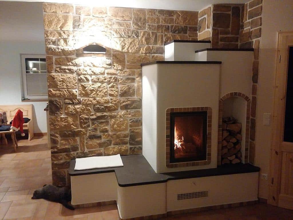 Speicherofen mit Kamin in rustikalem Wohnzimmer, eingebaut in eine Wand aus Naturstein.