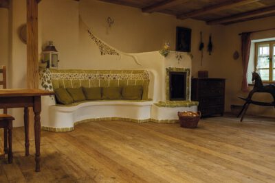 07-Ambio-Speicher_und-Grundofen Grundofen mit geschwungener Sitzbank und Naturstein-Details in rustikalem Wohnraum